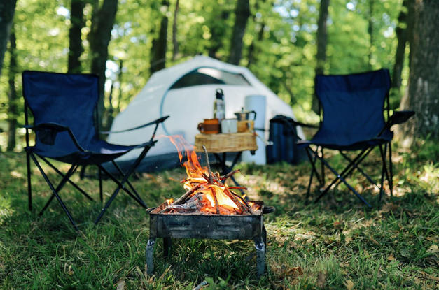 Campement en pleine nature avec tente, feu de camp et chaises pliantes