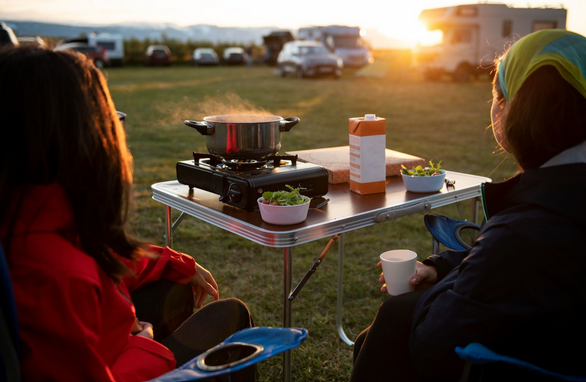 Deux femmes qui mangent sur un emplacement de camping avec caravane en regardant le couché du soleil.