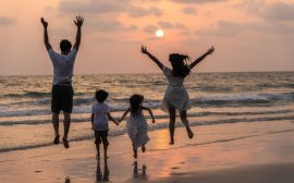 Famille en vacances sur la plage au coucher du soleil, parents et enfants sautant et courant ensemble face à la mer, ambiance joyeuse et conviviale idéale pour illustrer des vacances en camping en famille.