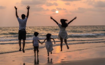 Famille en vacances sur la plage au coucher du soleil, parents et enfants sautant et courant ensemble face à la mer, ambiance joyeuse et conviviale idéale pour illustrer des vacances en camping en famille.