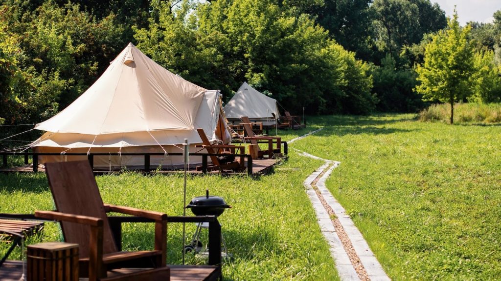 Tentes de glamping dans un camping en pleine nature, avec chaises en bois et allée aménagée