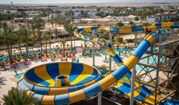 Grand parc aquatique de camping avec toboggans colorés, piscine et transats entourés de palmiers.